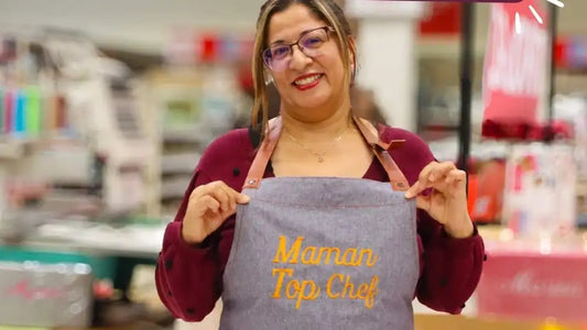 Femme souriante portant un tablier brodé gris avec inscription 'Maman Top Chef', cadeau personnalisé