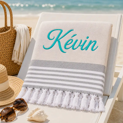 Fouta_personnalisee_beige_naturel_brodee_au_prenom_Kevin_en_fil_turquoise_serviette_plage_coton_turc_a_franges_sur_transat