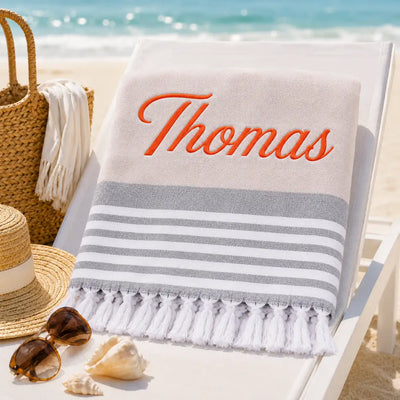Fouta_personnalisee_beige_naturel_brodee_au_prenom_Thomas_en_fil_orange_serviette_plage_coton_turc_a_franges_sur_transat
