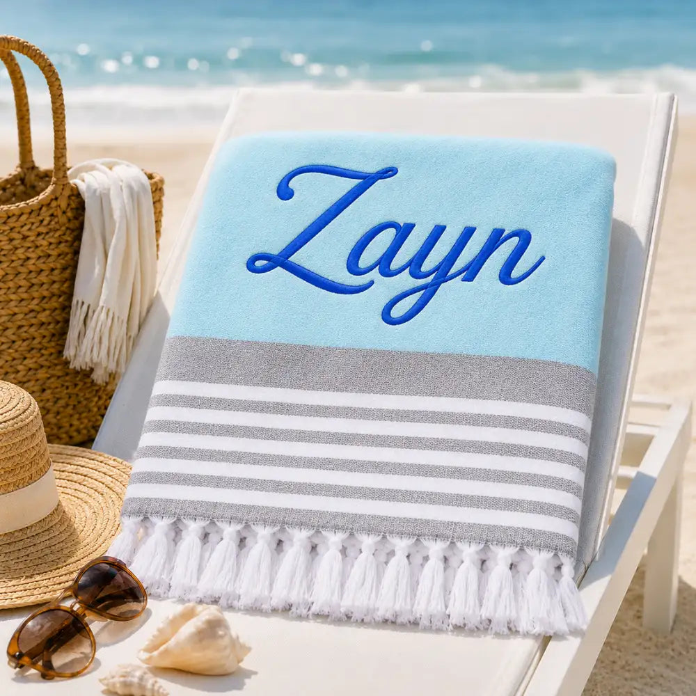 Fouta personnalisée bleu ciel brodée au prénom Zayn en fil bleu roi, serviette plage coton turc à franges sur transat
