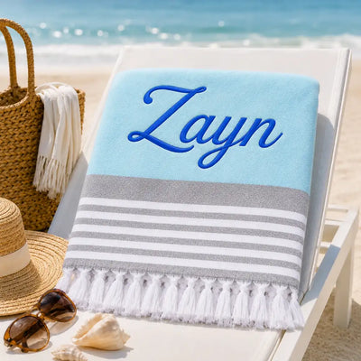 Fouta personnalisée bleu ciel brodée au prénom Zayn en fil bleu roi, serviette plage coton turc à franges sur transat
