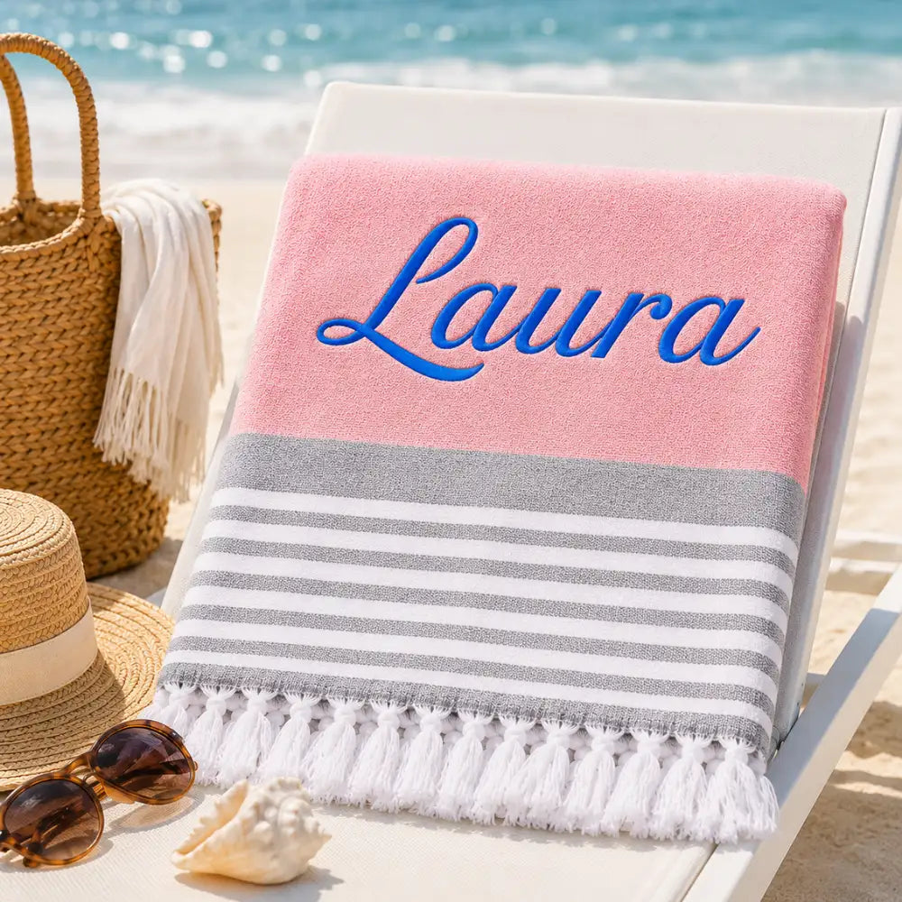 Fouta personnalisée rose brodée au prénom Laura en fil bleu, serviette plage coton turc à franges sur transat