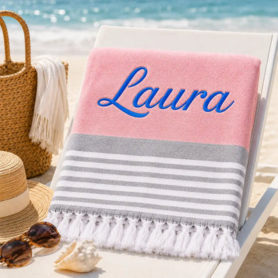 Fouta personnalisée rose brodée au prénom Laura en fil bleu, serviette plage coton turc à franges sur transat