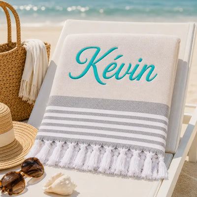 Fouta_personnalisee_beige_naturel_brodee_au_prenom_Kevin_en_fil_turquoise_serviette_plage_coton_turc_a_franges_sur_transat