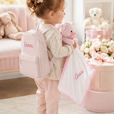 Petite fille portant son sac à dos rose brodé Enora et tenant son doudou ourson assorti brodé au prénom